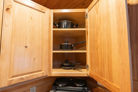 Wooden kitchen cabinet with cookware neatly organized on shelves.