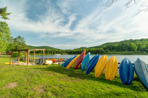 Colorful kayaks lined up by a peaceful lake with forested hills in the background