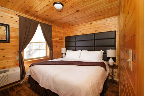 Cozy bedroom with wood-paneled walls and a large bed featuring a dark upholstered headboard.