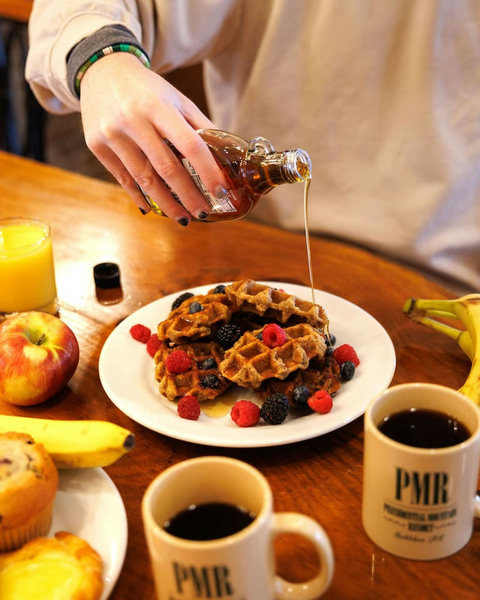 Enjoy a cozy breakfast with waffles, fresh berries, coffee, and fruit on a wooden table.