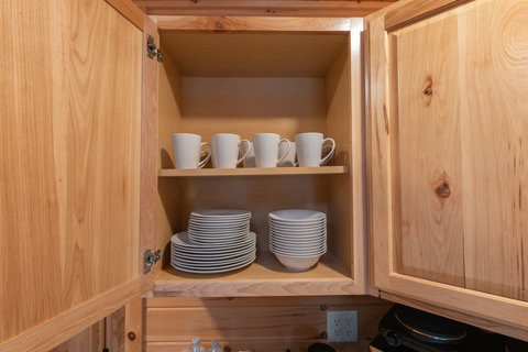 organized wooden cabinet with white mugs, plates, and bowls