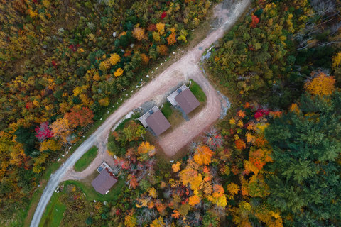 Aerial view of three cabins surrounded by colorful autumn forest.