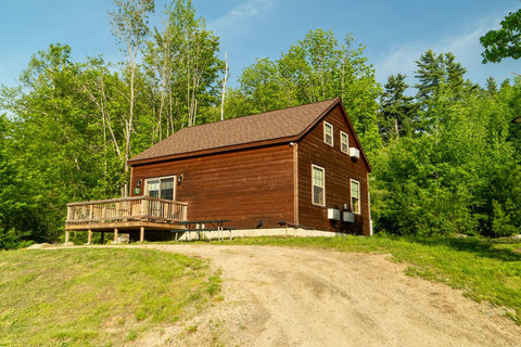 Rustic cabin surrounded by lush green trees with a wooden deck for outdoor relaxation.