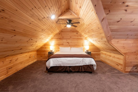 Cozy attic bedroom with wood paneling and a ceiling fan for a rustic retreat.