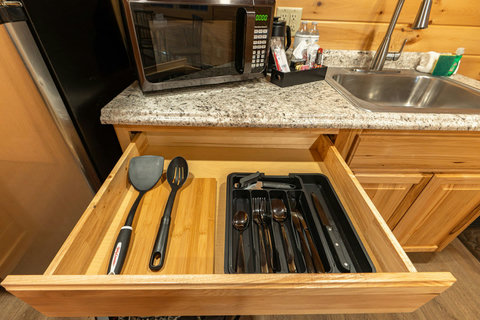 Organized kitchen drawer with utensils and a microwave on granite countertop in a rustic-style kitchen.
