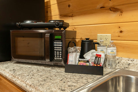 Compact kitchen area with microwave, hot plate, and coffee supplies on a granite countertop.