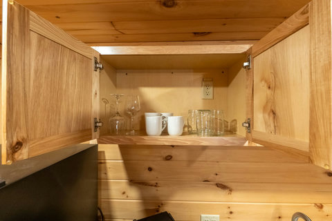 Open wooden cabinet with glassware and mugs in a rustic kitchen setting