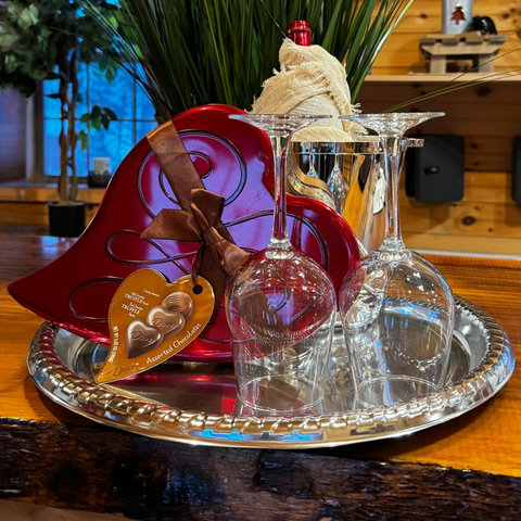 Romantic setup with wine glasses, chocolates, and a bottle on a silver tray in a cozy wooden interior.
