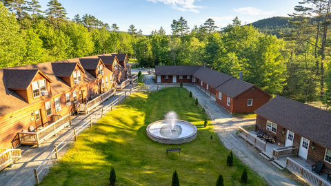 Rustic lodge cabins surround a central fountain in a peaceful forest setting.