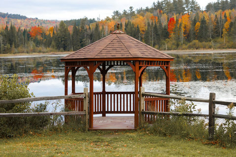 Rustic wooden gazebo overlooking a serene lake surrounded by autumn foliage.