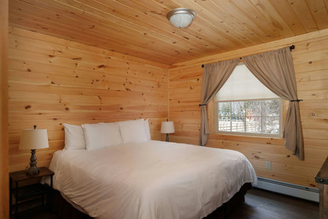 Cozy bedroom with wood-paneled walls and a large window for natural light