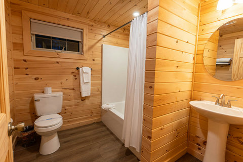 Rustic bathroom with wood-paneled walls, a bathtub with shower curtain, and a pedestal sink.