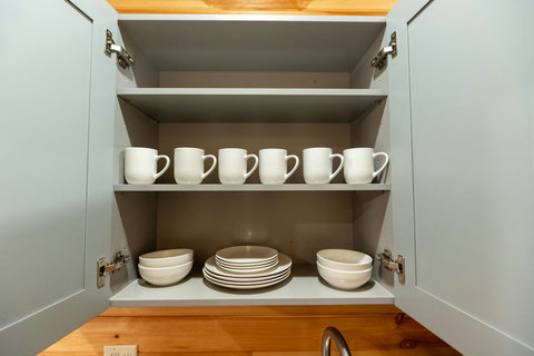 organized kitchen cabinet with white mugs, plates, and bowls