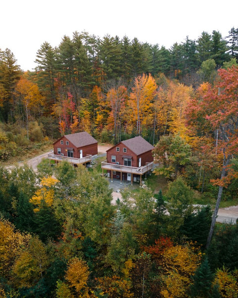 Two rustic cabins surrounded by vibrant autumn forest foliage