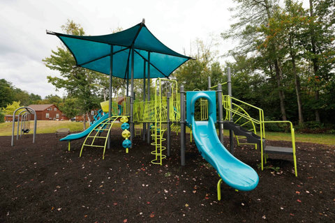 Outdoor playground with slides and swings surrounded by trees and cabins.