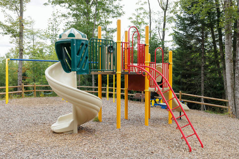 Playground with a spiral slide and climbing ladder set in a wooded area for family-friendly outdoor fun.
