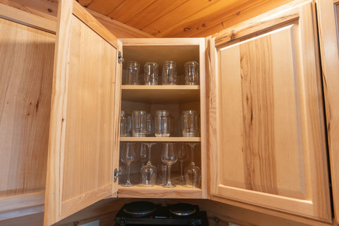 Open wooden cabinet displaying a variety of glassware including mason jars and wine glasses.