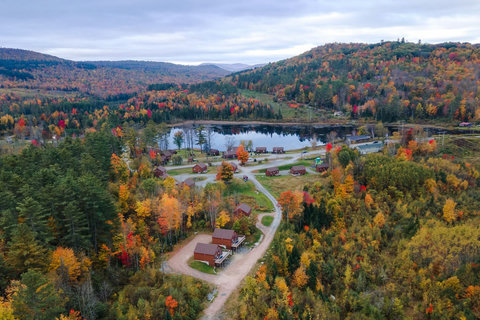 Rustic cabins nestled among colorful autumn trees with a serene lake and rolling hills in the background.