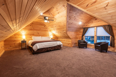Spacious attic bedroom with wood-paneled walls and a cozy seating area by the window.