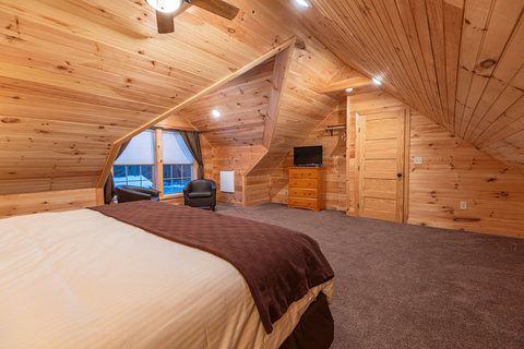 Cozy attic bedroom with wood paneling and a seating area by the window