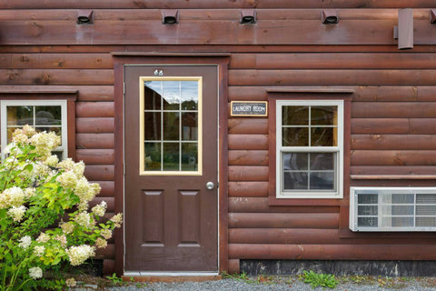 Exterior view of the rustic laundry room entrance with natural wood siding and flowering shrubs.