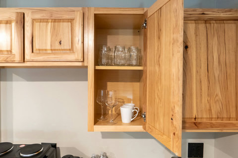 Open kitchen cabinet showcasing glassware and mugs in a natural wood finish.