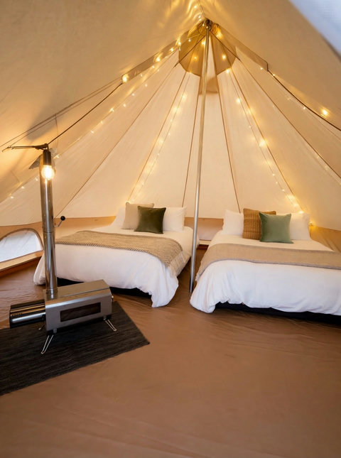 Interior of a glamping tent featuring two beds, string lights, and a wood stove for cozy warmth.