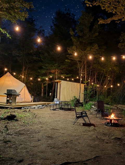 Rustic campsite with string lights, a fire pit, and a tent under a starry night sky