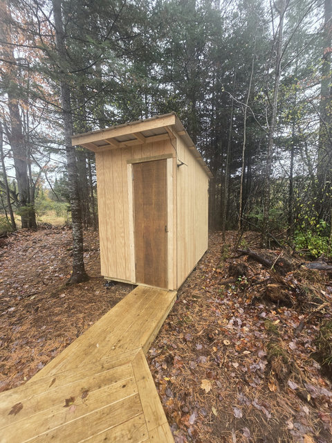 rustic wooden shed surrounded by forest with a wooden walkway leading to the door