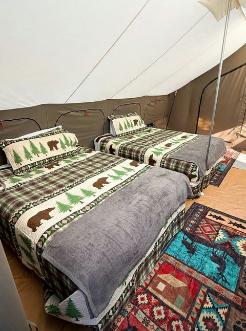 Spacious glamping tent interior featuring twin beds with forest-themed bedding and comfortable rocking chairs.