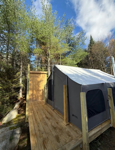 Rustic canvas tent on a wooden platform surrounded by autumn forest foliage.