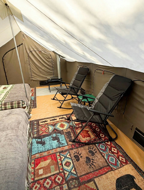 Spacious glamping tent interior featuring twin beds with forest-themed bedding and comfortable rocking chairs.