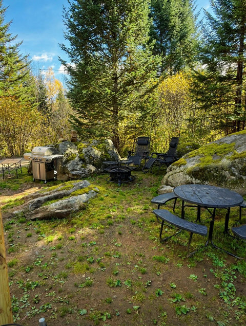 Outdoor picnic area surrounded by forest with a stone cairn and string lights for a peaceful retreat.