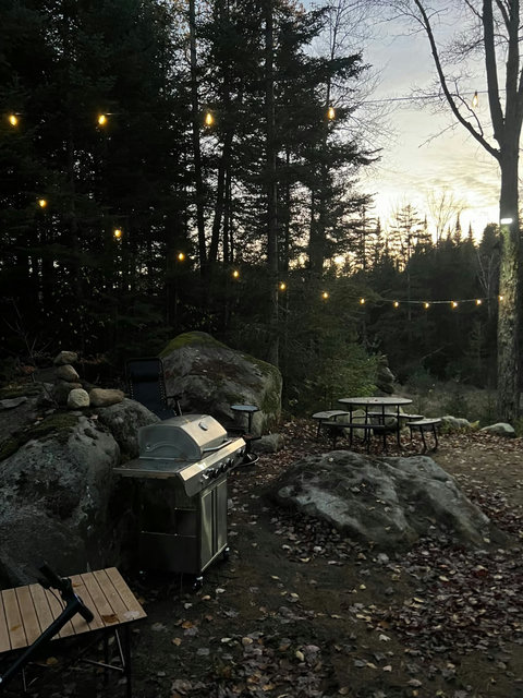 Outdoor grilling area with a stainless steel barbecue and a fire pit surrounded by natural rock formations.