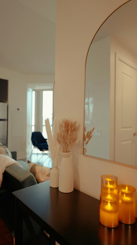 A chic entry table adorned with moody, flickering candles, sleek vases filled with soft pampas grass, and an elegant mirror that reflects the warm, sophisticated ambiance.