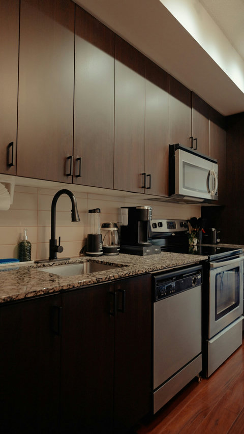 A sleek modern kitchen features seamless cabinetry and stainless steel appliances, including a built-in dishwasher, oven, gas stove, microwave, and a refrigerator-freezer.